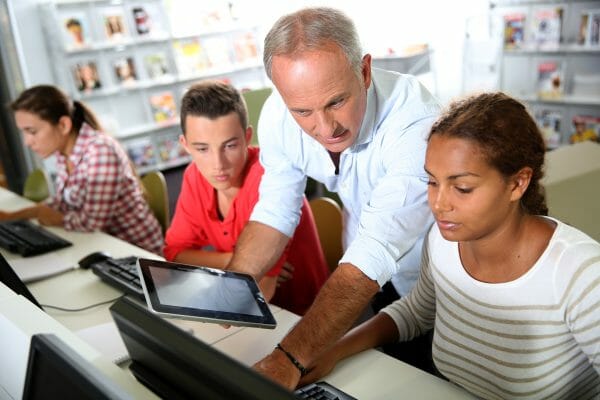 Older male teacher showing students something on a computer